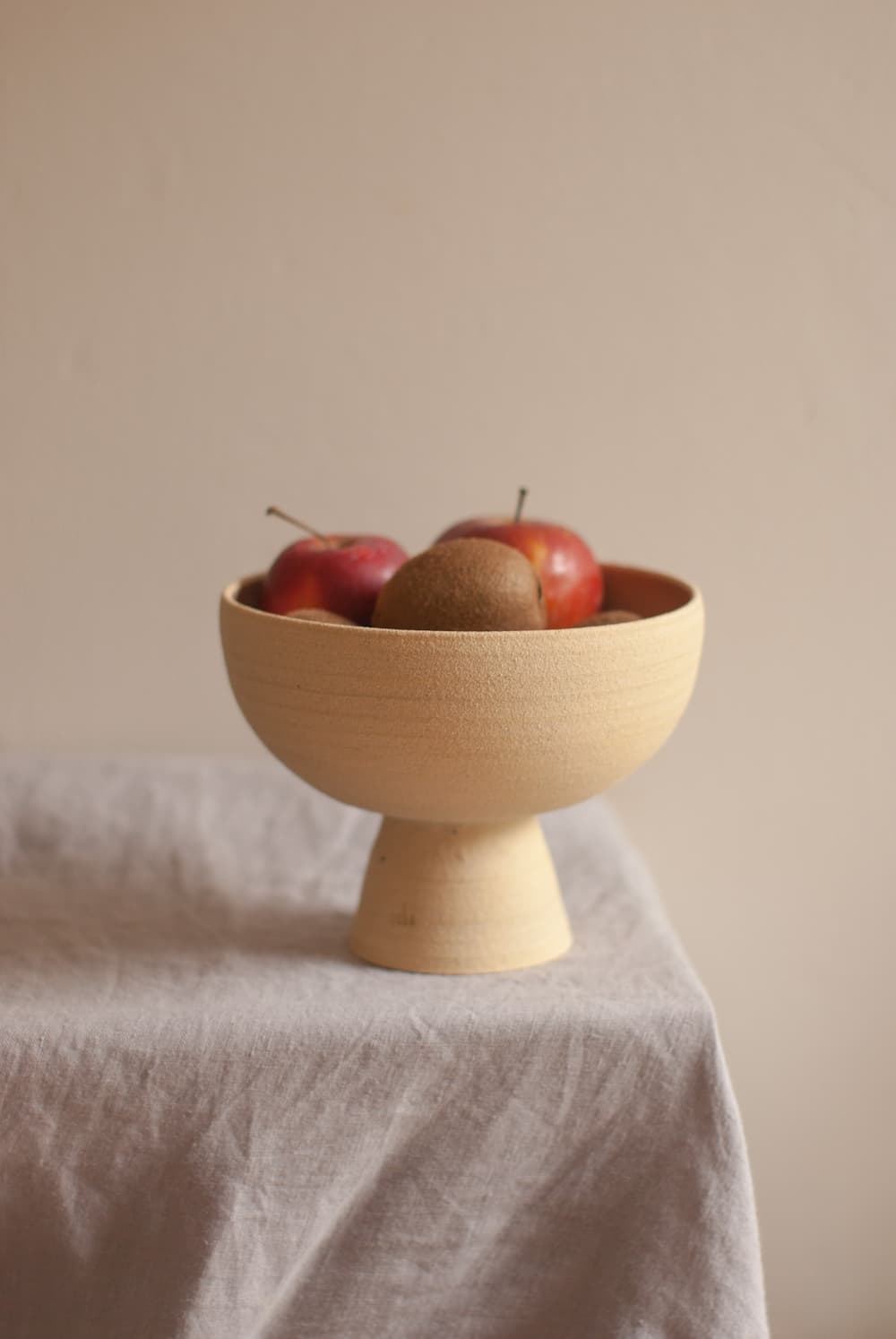 A wooden bowl filled with apples resting on   the   corner of a table that is draped in a grey tablecloth.